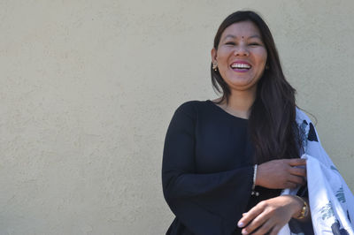 Portrait of a smiling young woman standing against wall