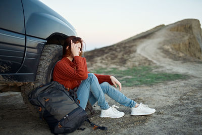 Young woman sitting on car against mountain