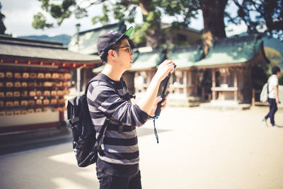 Man holding monopod while standing on footpath in city