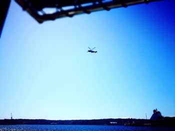 Low angle view of airplane flying over sea against clear blue sky