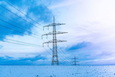 Low angle view of electricity pylon against sky during winter