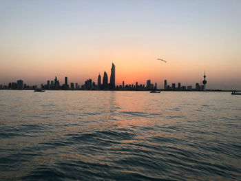 Scenic view of sea and buildings against sky during sunset asides kuwait city with kuwait tower.