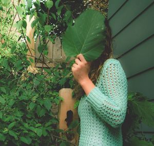 Side view of young woman hiding face with leaf in back yard