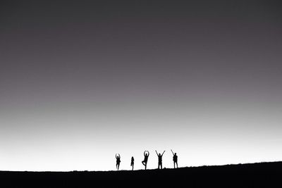 Low angle view of silhouette friends posing on field against clear sky