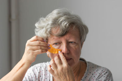 Senior woman applying hydrogel eye patches against wrinkles. gray-haired lady using cosmetics.