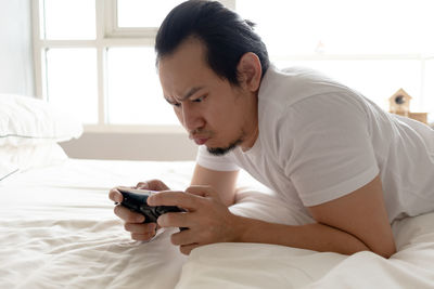 Young man using mobile phone while sitting on bed at home