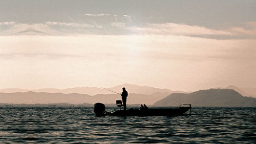 Silhouette man in sea against sky during sunset