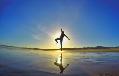 Silhouette of man jumping at beach against sky during sunset