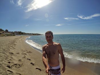 Portrait of shirtless man standing at beach against sky