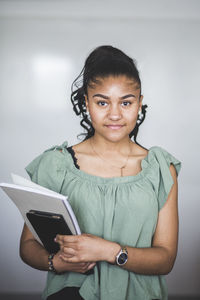 Portrait of confident teenage girl standing with book against whiteboard in computer lab at high school