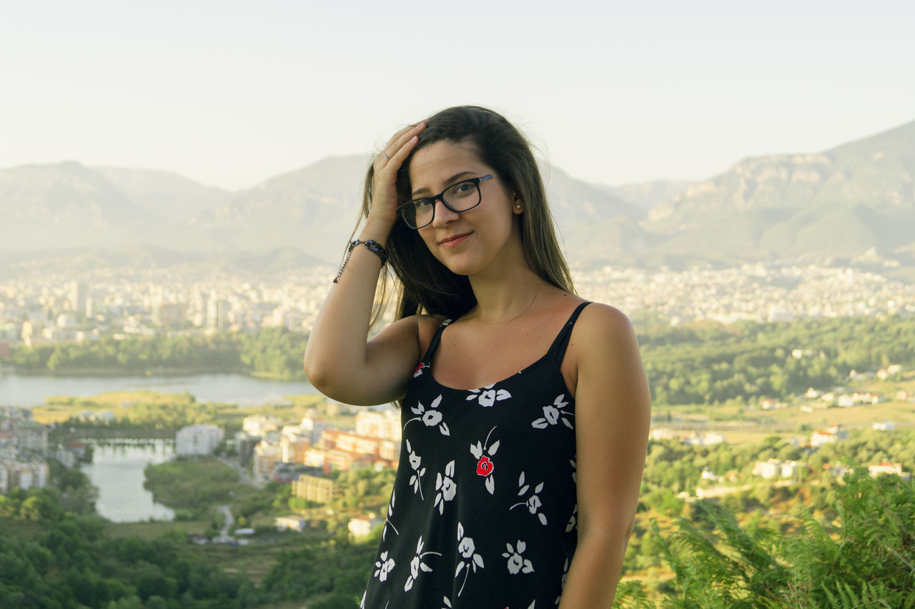 Portrait of young woman standing against cityscape