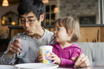 Father with daughter having drinks while sitting at table in cafe