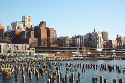 Wooden posts in hudson river by buildings against clear sky