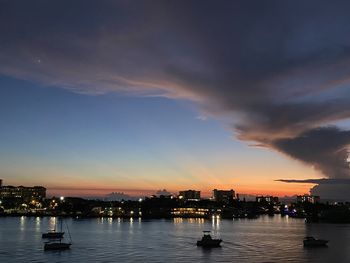 Illuminated city by river against sky during sunset