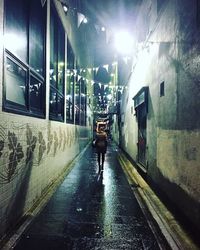 Rear view of man walking on illuminated road