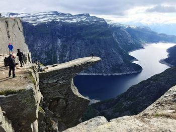 People on rocky cliff against mountains