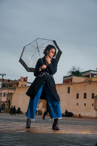 Full length of young woman holding umbrella in rain
