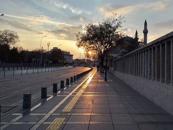 Footpath by street against sky during sunset