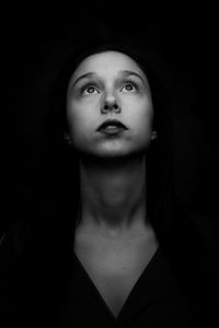 Close-up of beautiful young woman looking up over black background