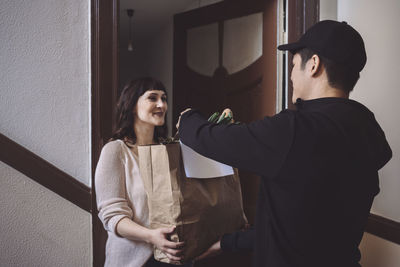 Smiling customer talking to delivery man while holding vegetable bag at doorstep