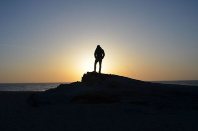 Silhouette man standing on rock by sea against sky during sunset