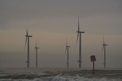 Windmills on beach against sky during sunset