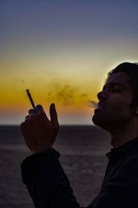 Man smoking cigarette against sky during sunset