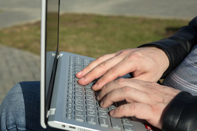 Male hands on a laptop keyboard typing text, the concept of a freelancer's work in the fresh air.