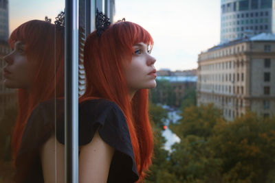 Close-up of beautiful woman with redhead looking through window