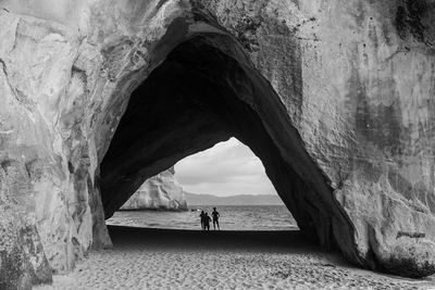 Black and white group of people in cathedral cave silhouetted against the sea and beach.