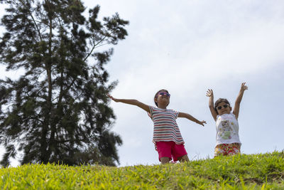 Low angle view of sisters playing on grass against sky