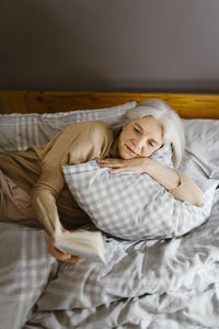 Senior woman reading book while lying on bed at home