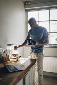 Male entrepreneur pouring coffee in paper cup while standing near table at workshop