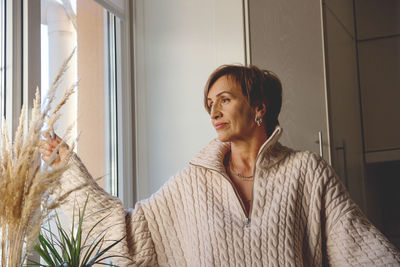 Young woman looking through window at home