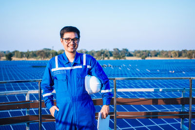 Portrait of smiling young man standing against blue sky