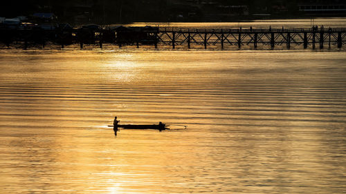 Silhouette people on boat in river at sunset