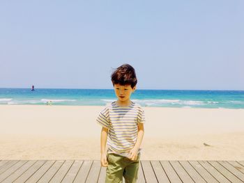 Boy on boardwalk at beach against clear sky