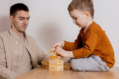 Father and son sitting together at home and playing with wooden blocks. jenga game. 