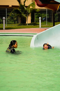 Children sliding into pool after going down water slide during summer.