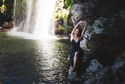 Woman sitting on rock by waterfall in forest