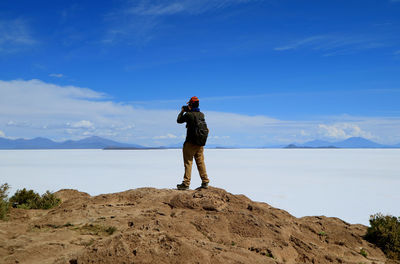 Rear view of man photographing salt flat against blue sky