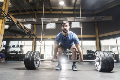 Man looking away while picking barbell at gym