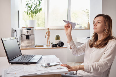 Woman plays with paper plain at home office. procrastinate at remote work