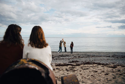 Rear view of couple looking at friends enjoying on sea shore