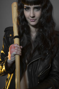 Portrait of young female model holding baseball bat against gray background