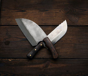 Metal sharp kitchen knives in a wooden handle on a brown table made of boards, top view