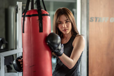 Portrait of confident young woman practicing boxing with punching bag in gym