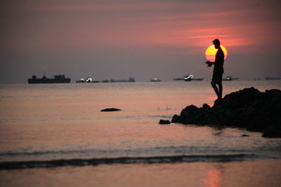 Silhouette man standing on beach against sky during sunset