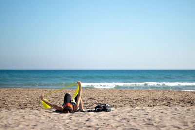 Adult woman exercising with rubber bands on the beach lying down on the beach