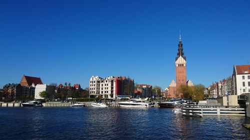 Boats moored in city against clear blue sky